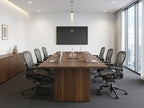 Walnut conference table in a corporate boardroom with a wall-mounted display, laptops and gray mesh chairs